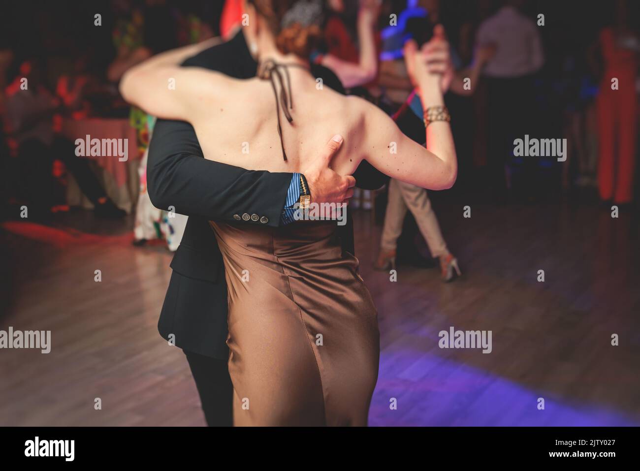Couples dancing traditional latin argentinian dance milonga in the ballroom, tango salsa bachata kizomba lesson in the red and purple lights, dance fe Stock Photo