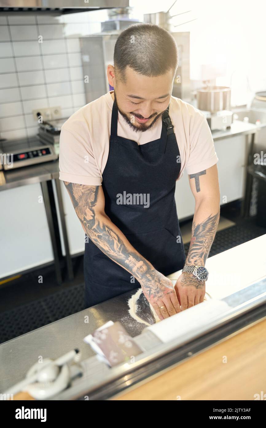 Pleasant Asian guy working in the kitchen and making dough Stock Photo