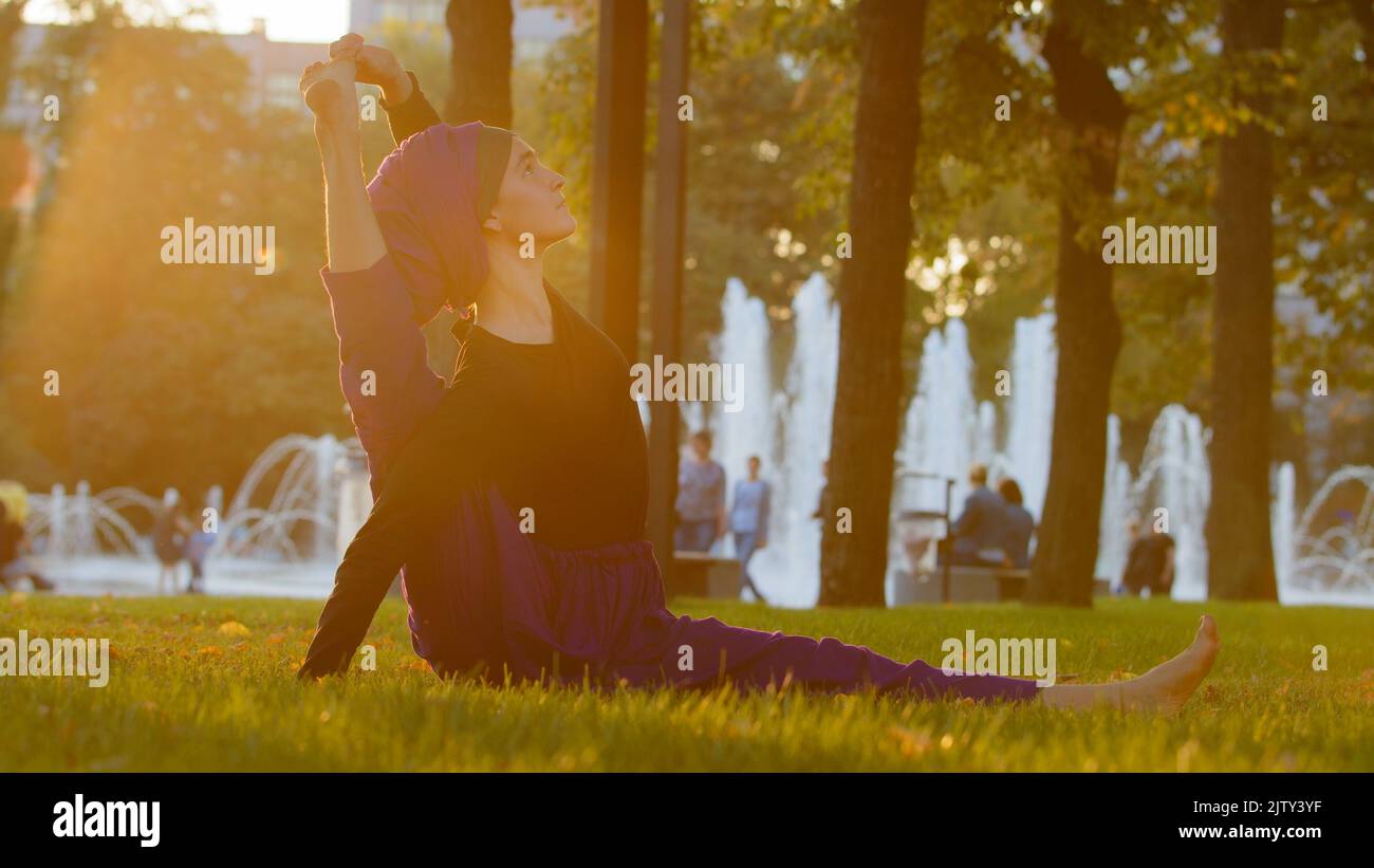 Strong islamic muslim indian woman in hijab active girl doing yoga in park outdoors training exercises tensing muscles showing acrobatic elements Stock Photo