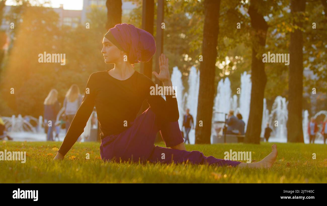 Strong islamic muslim indian woman in hijab active girl doing yoga in park outdoors training exercises tensing muscles showing acrobatic elements Stock Photo