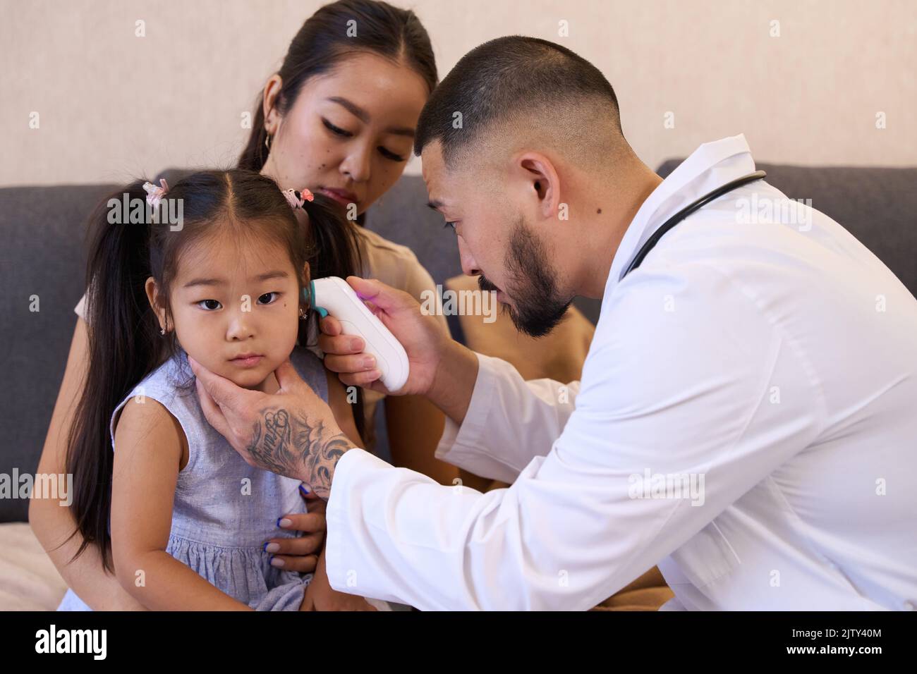 Caring otolaryngologist doctor looking through otoscope at Asian girl