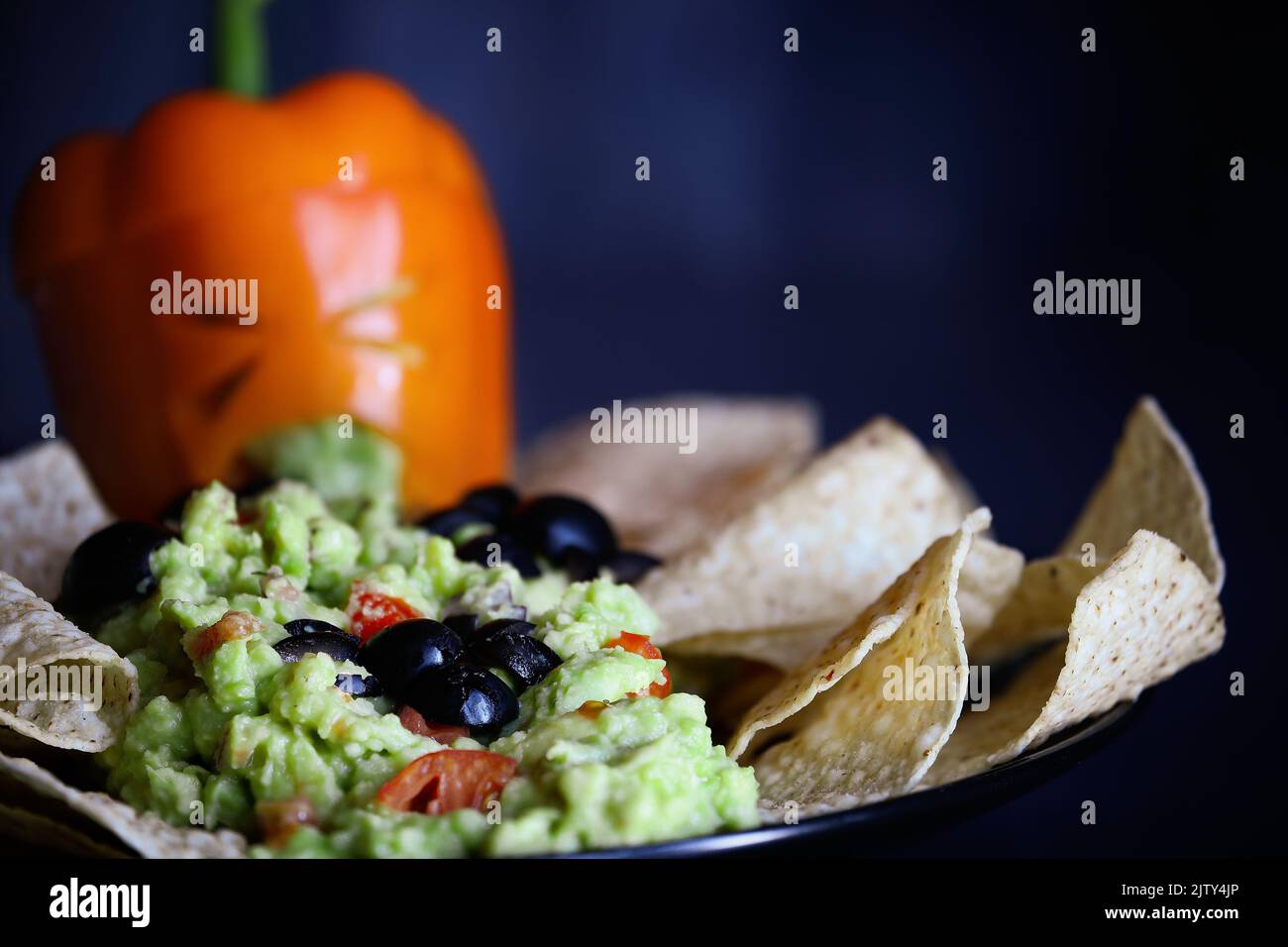 Black olive spiders crawling on guacamole with chips. Selective focus on bug with blurred foreground and background. Pepper as monster with cut out fa Stock Photo