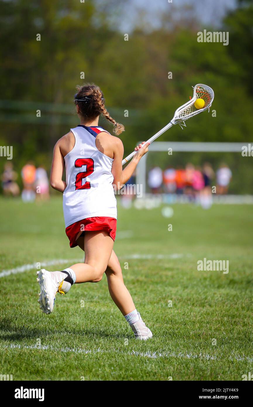 A rear view of a female lacrosse player running on the field with blurred background Stock Photo