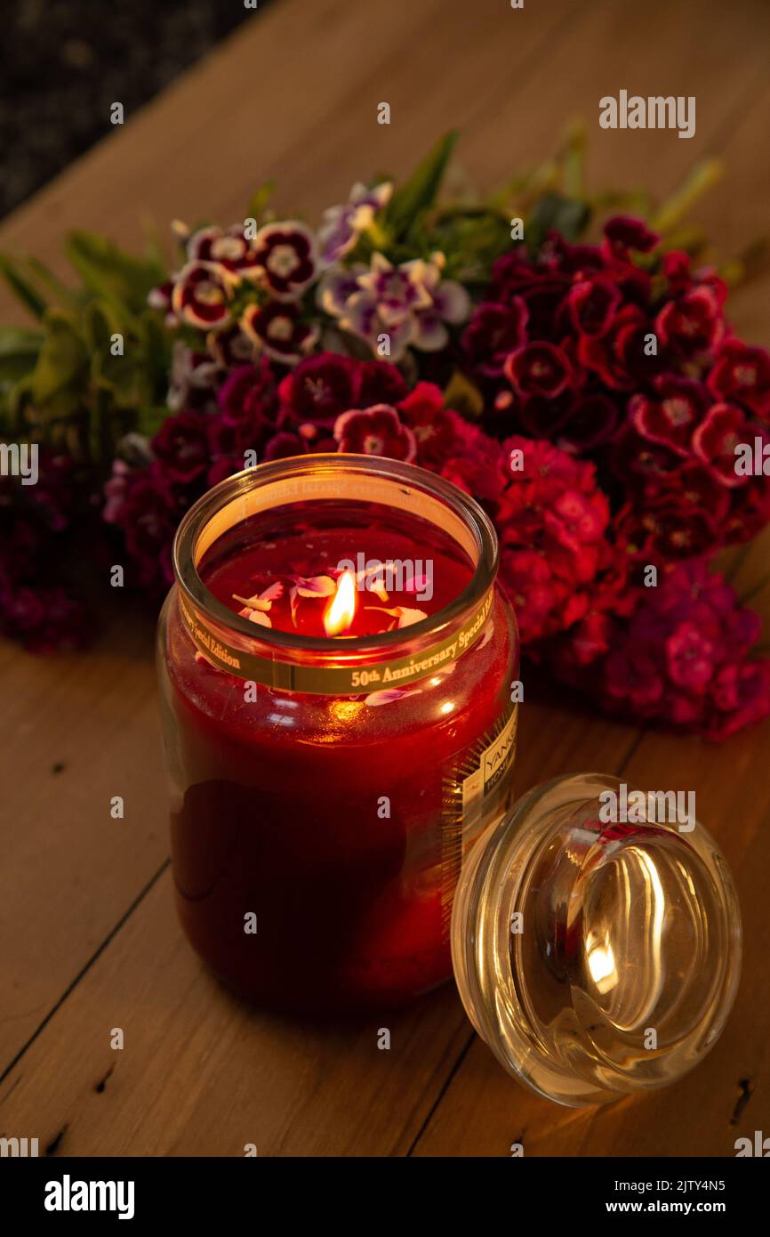 Yankee candle lit against a backdrop of flowers on a wooden board Stock Photo