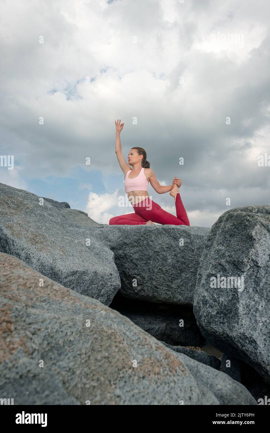 Fit, sporty woman practicing yoga on rocks, pigeon pose. Stock Photo