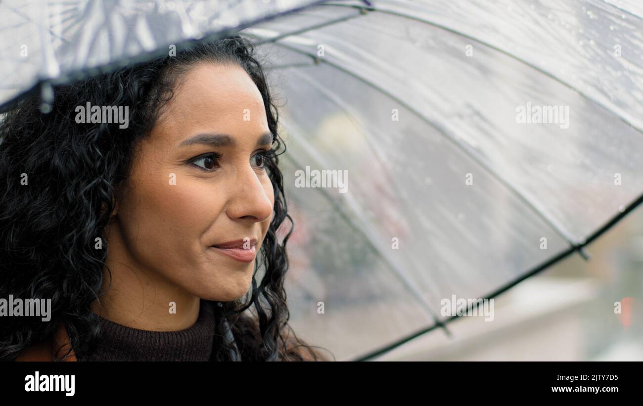 Portrait carefree attractive beautiful woman female happy hispanic girl with long dark curly hair holding transparent umbrella standing in city in Stock Photo