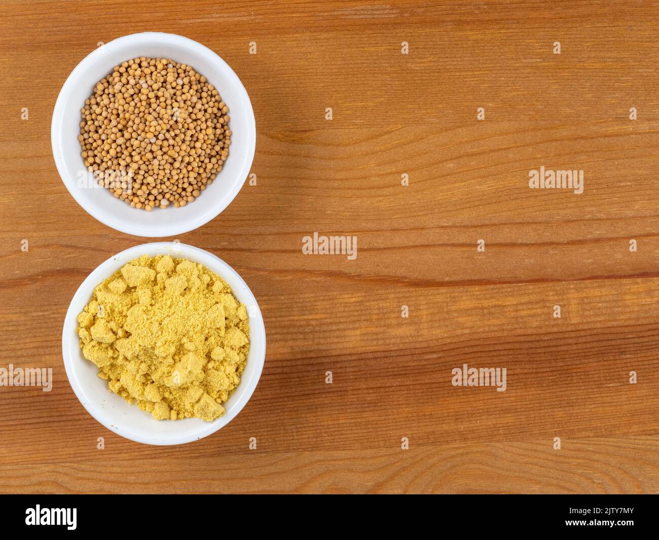 brown Mustard seeds and yellow mustard powder in white bowls on a wooden table Stock Photo