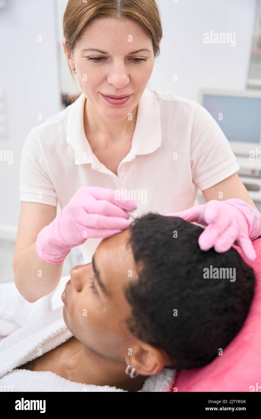 Cosmetologist placing markings on treatment area on young man face Stock Photo