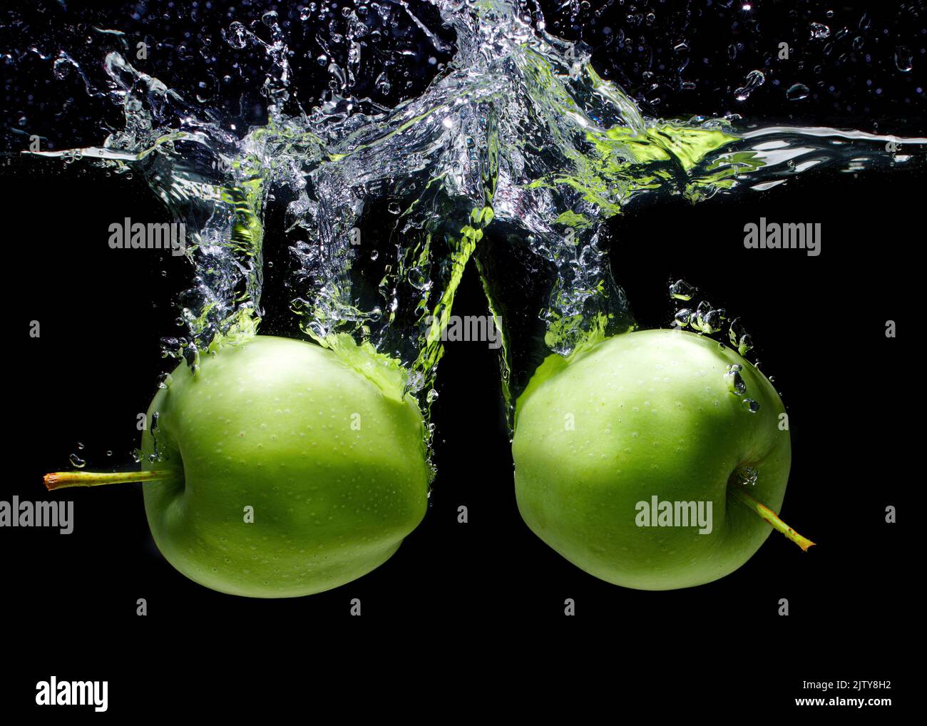 Green apples dropped in water with splashes and bubbles isolated on black background, close-up Stock Photo