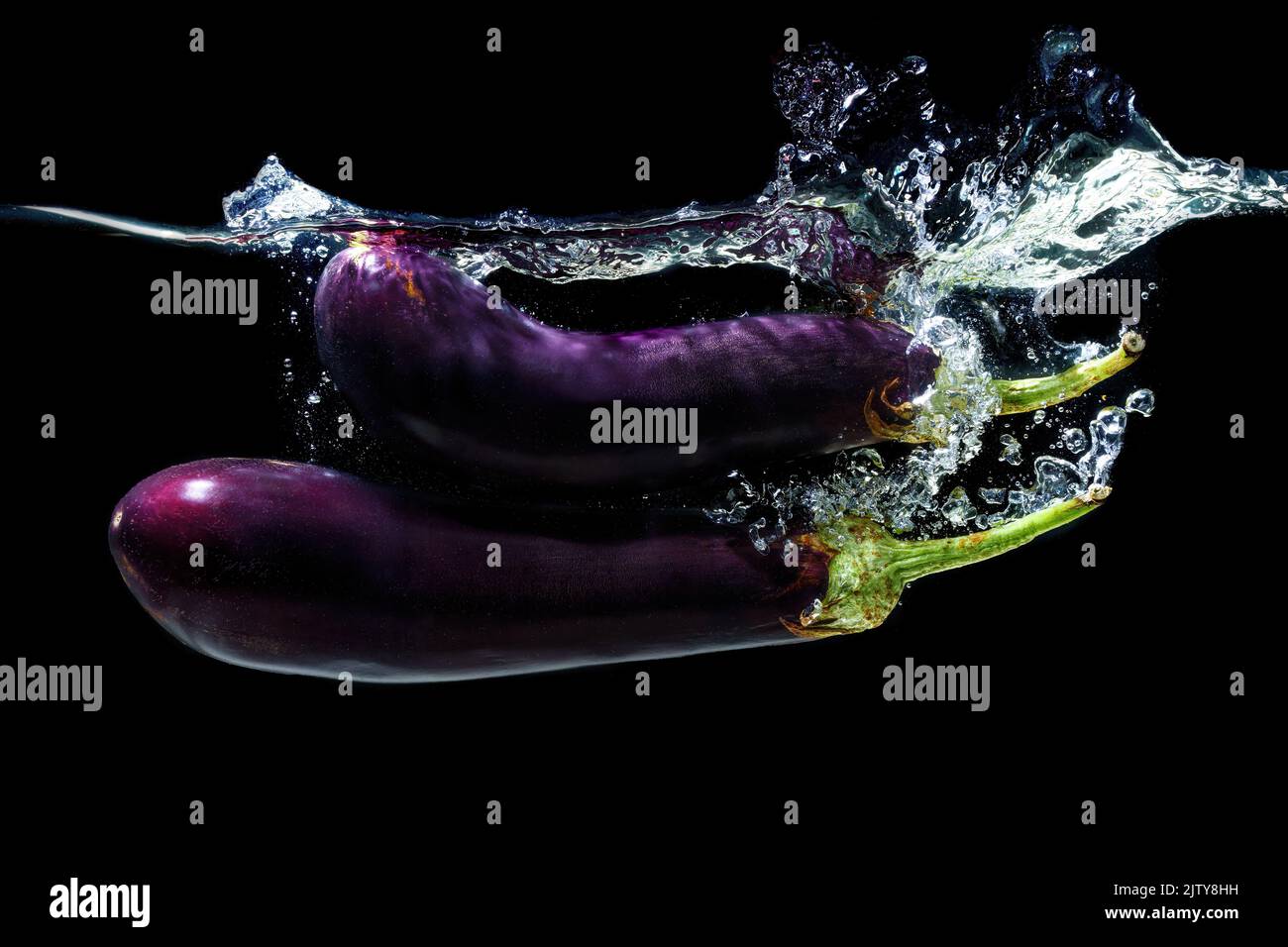 Two whole eggplants dropped in water with splashes on black Stock Photo