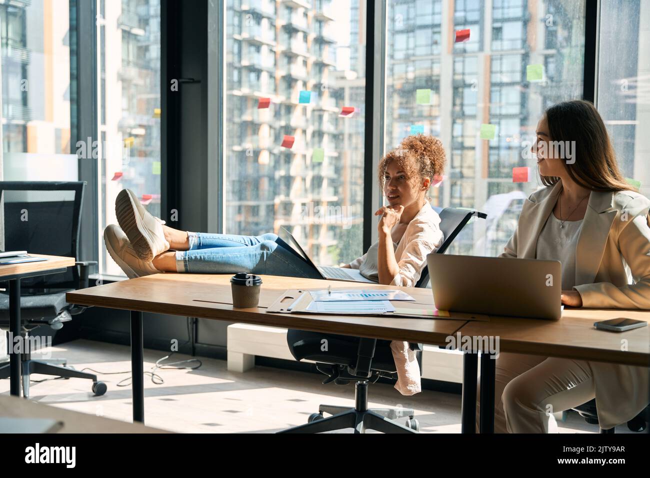 Joyful women chatting while working on laptop in coworking space Stock Photo