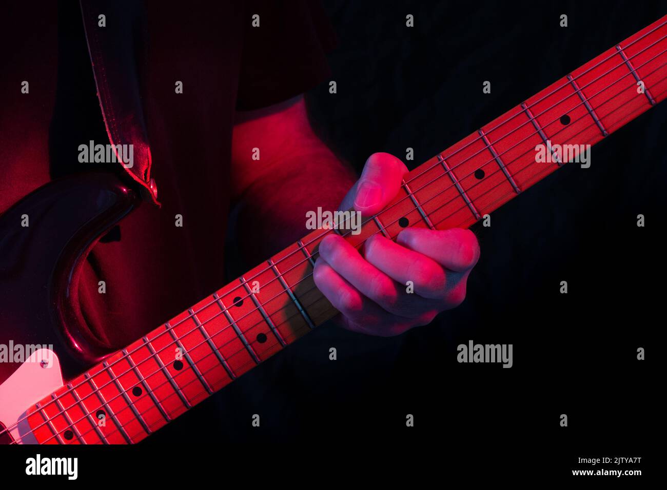 Electric guitar player in red stage lighting with dark to black background. Low key shot. Stock Photo