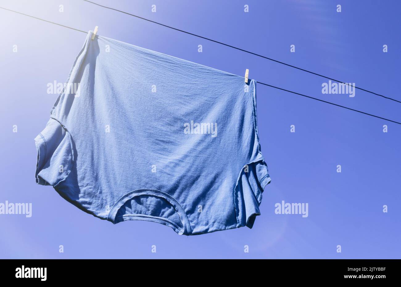 Blue T-shirt on laundry or clothes line with sun flare and copy space Stock Photo