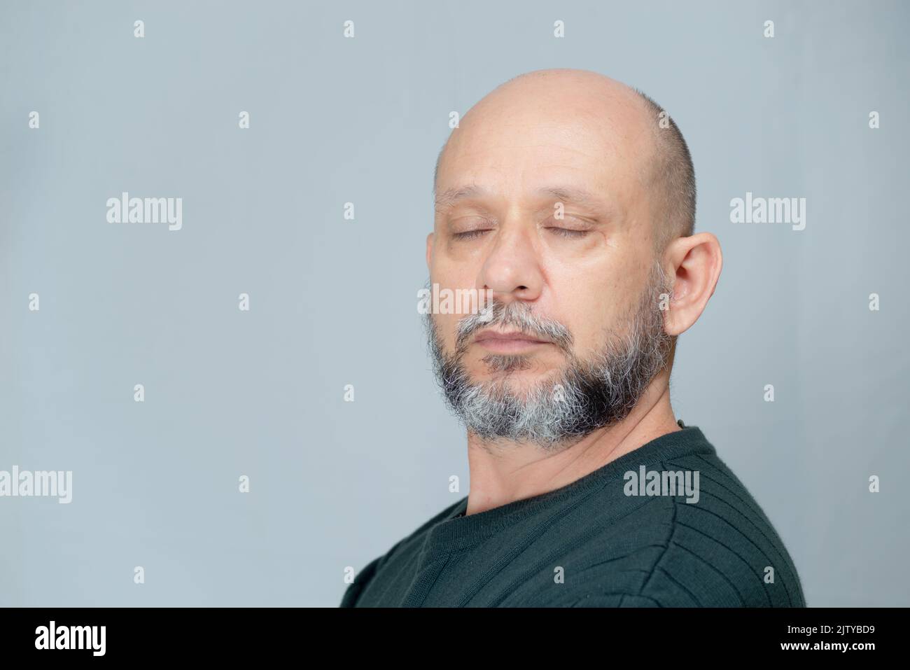 Portrait of mature man standing on light background. Bald bearded man with closed eyes. Formal style. Stock Photo