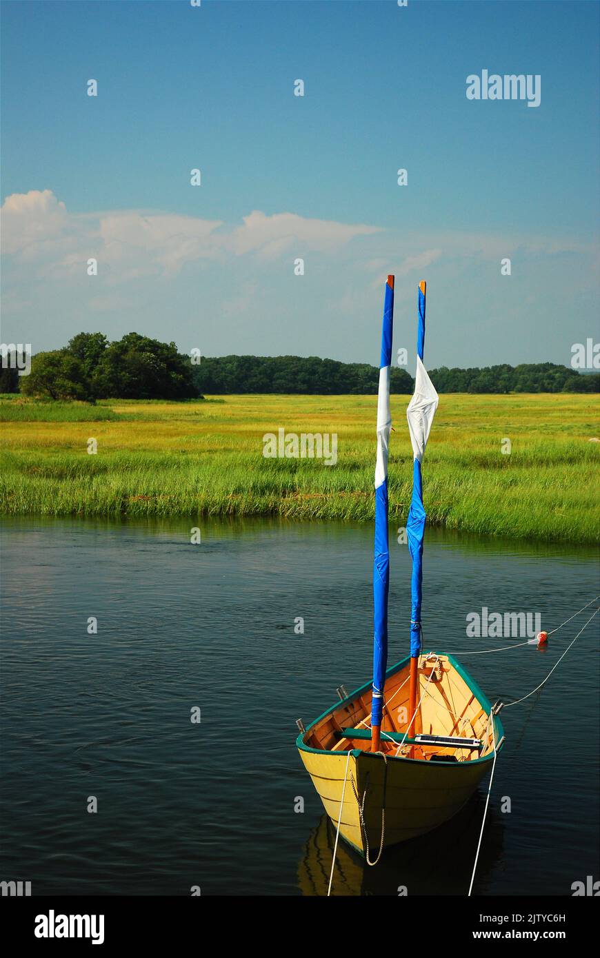 A small dinghy sailboat sits in a still water of a salt marsh Stock Photo
