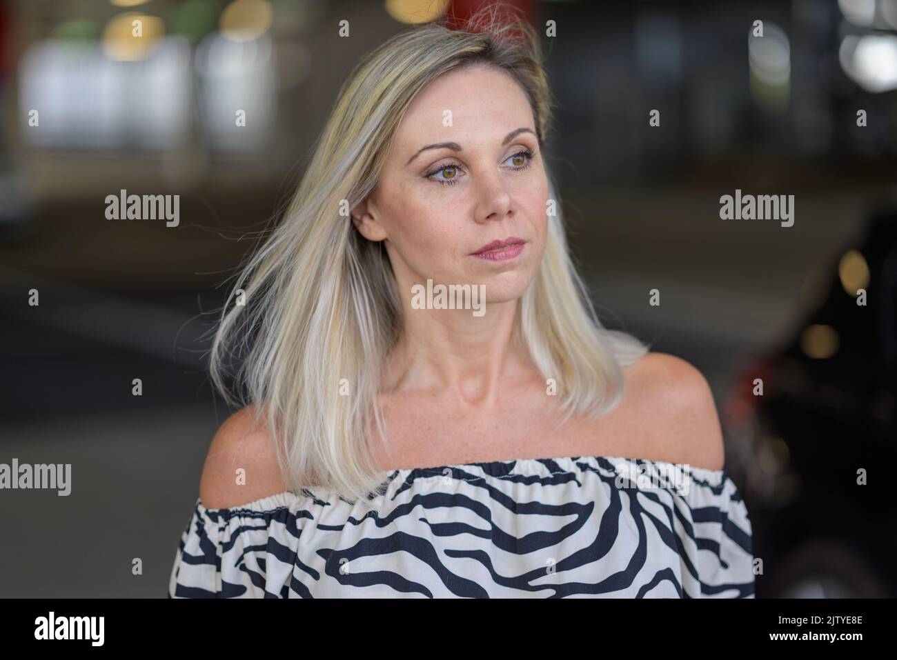 Thoughtful woman walking through an arcade or street at night looking to the side with a pensive expression in close up Stock Photo