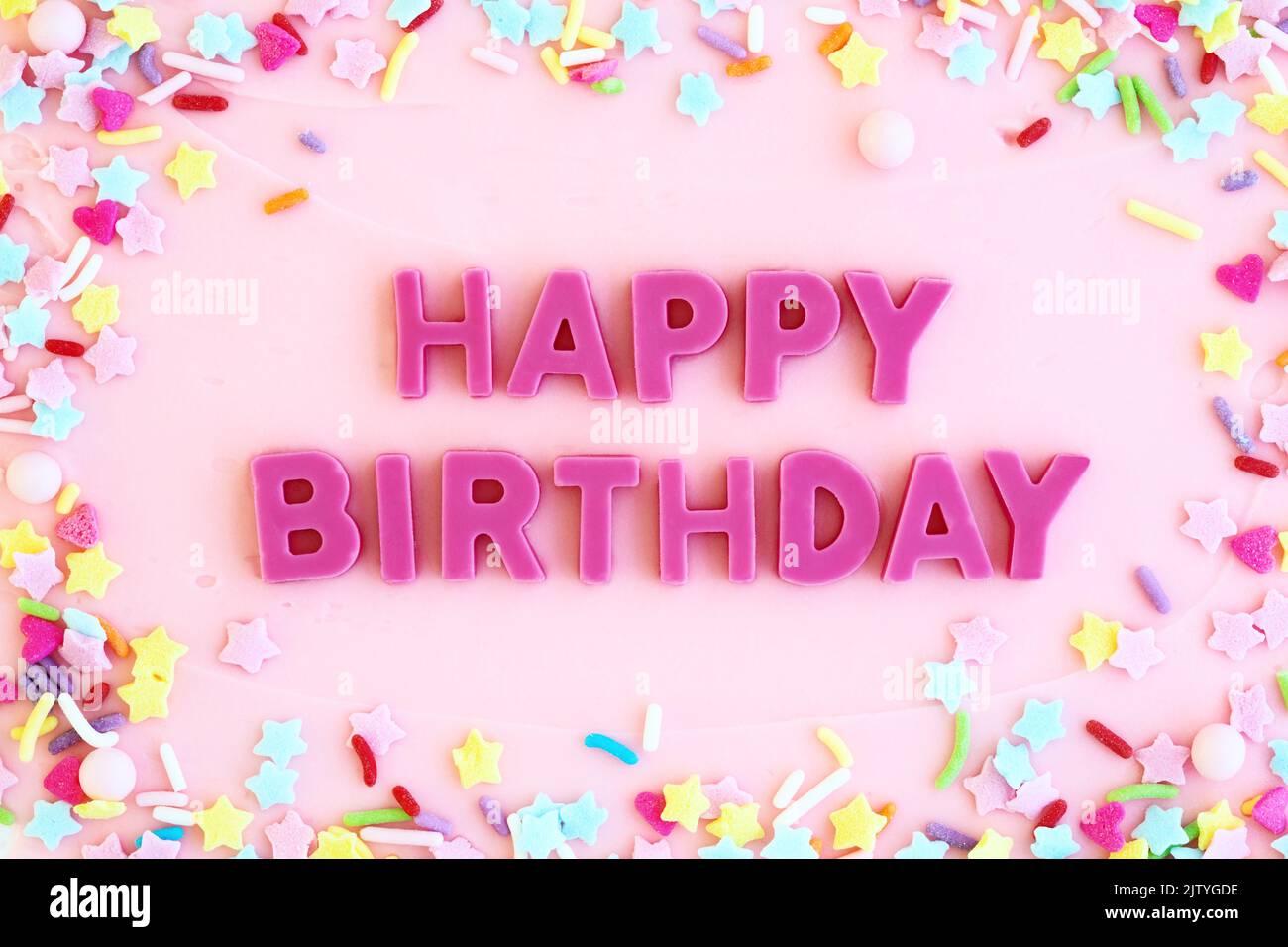 Pink frosted birthday cake with pink chocolate happy birthday message and sprinkles Stock Photo