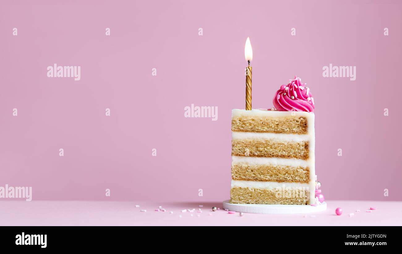 Slice of birthday cake with gold birthday cake candle and pink frosting on a pink background Stock Photo