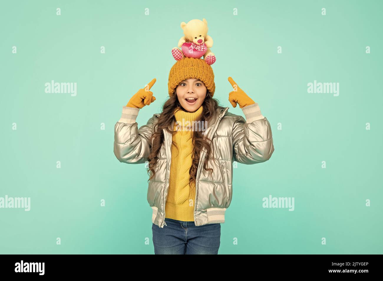 amazed child in hat and puffer jacket point finger on toy on blue background, toy shop. Stock Photo