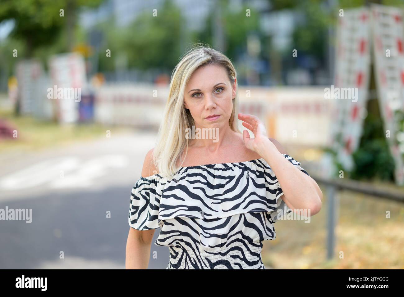 Serious blond woman walking down a quiet street with her hand raised to her hair looking thoughtfully at camera Stock Photo