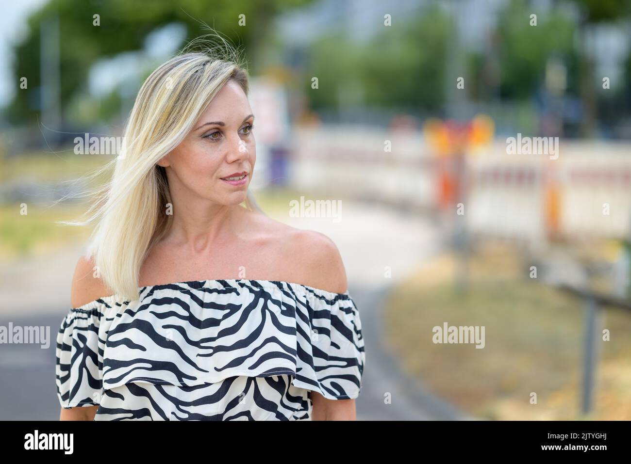 Woman walking down a quiet urban street looking aside with a thoughtful expression in close up Stock Photo
