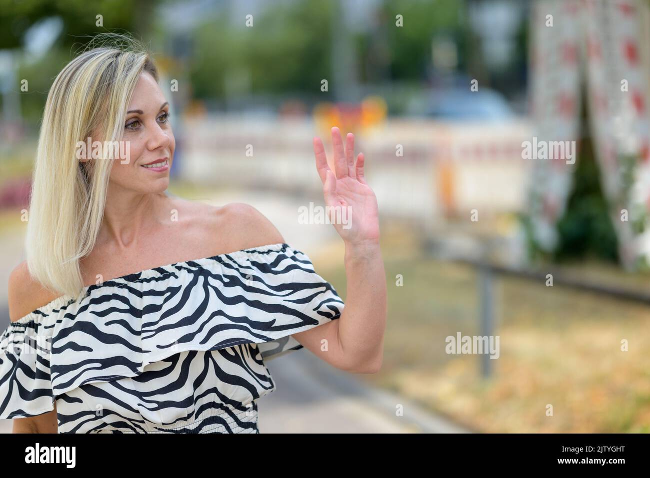 Woman waving at a friend as she walks down the street turning to the side with a quiet friendly smile Stock Photo