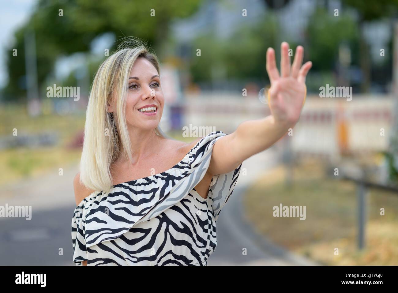 Animated attractive blond woman waving to a friend in the street with a look of delight Stock Photo