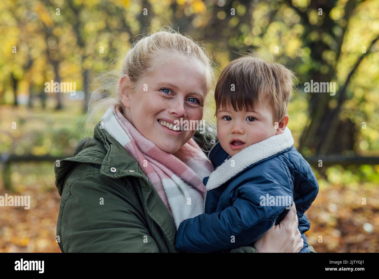 A mid adult woman carrying her baby boy in her arms while standing outside and embracing him in nature in Northumberland, North East England. They are Stock Photo