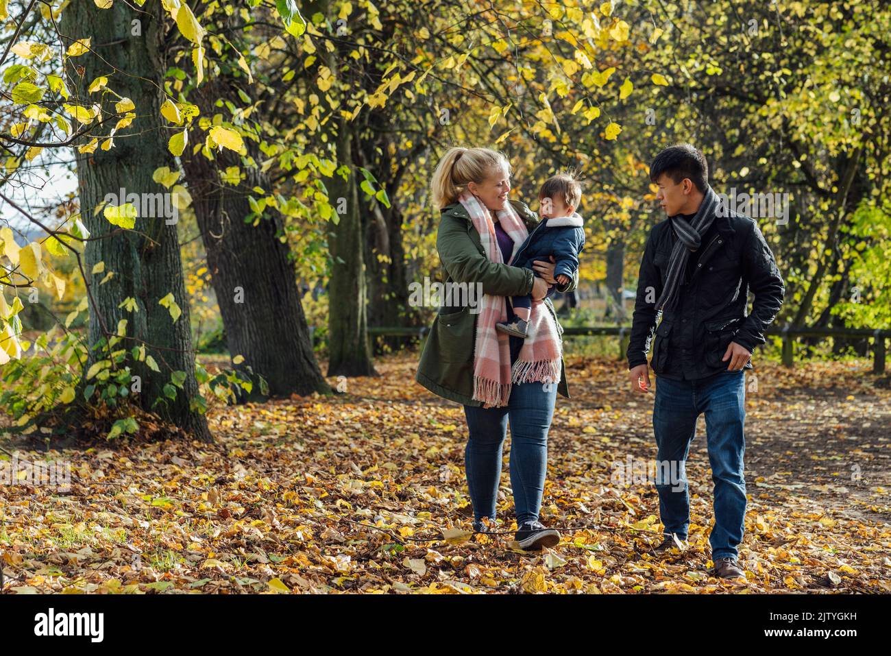 A couple walking through a park in nature Northumberland, North East England with their baby boy, who the woman is carrying in her arms. Stock Photo