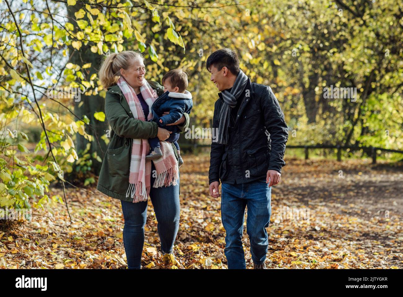 A couple walking through a park in nature Northumberland, North East England with their baby boy, who the woman is carrying in her arms. They are laug Stock Photo