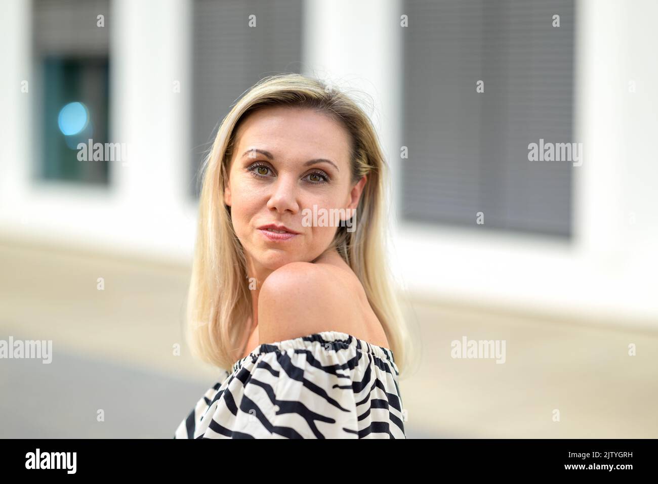 Pretty middle aged blond woman turning to look at the camera with a smile in a close up outdoor portrait Stock Photo