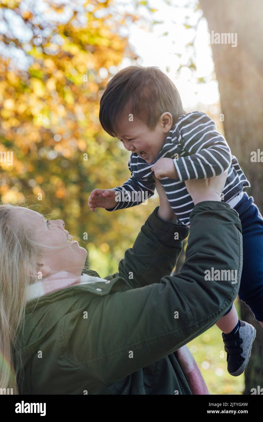 A mid adult woman holding  her baby boy up in the air while standing outside in nature in Northumberland, North East England. They are looking at each Stock Photo