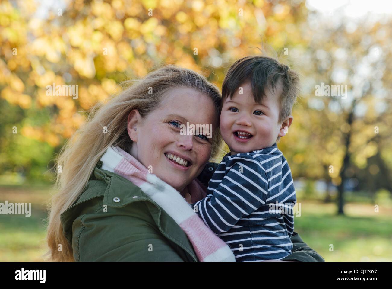 A mid adult woman carrying her baby boy in her arms while standing outside and embracing him in nature in Northumberland, North East England. They are Stock Photo