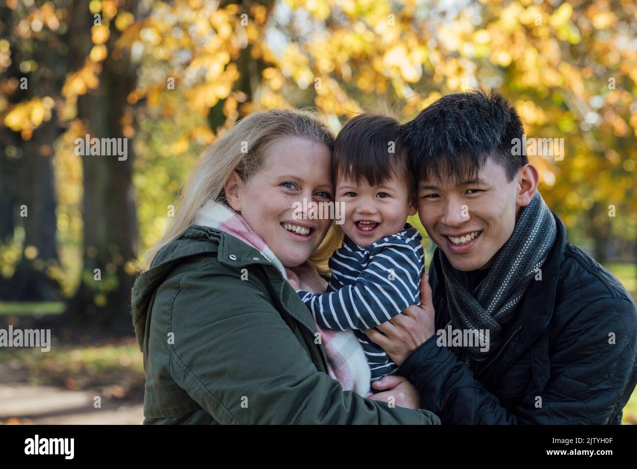 A family standing together outdoors in nature in Northumberland, North East England. They are carrying and cuddling their baby boy while they all look Stock Photo