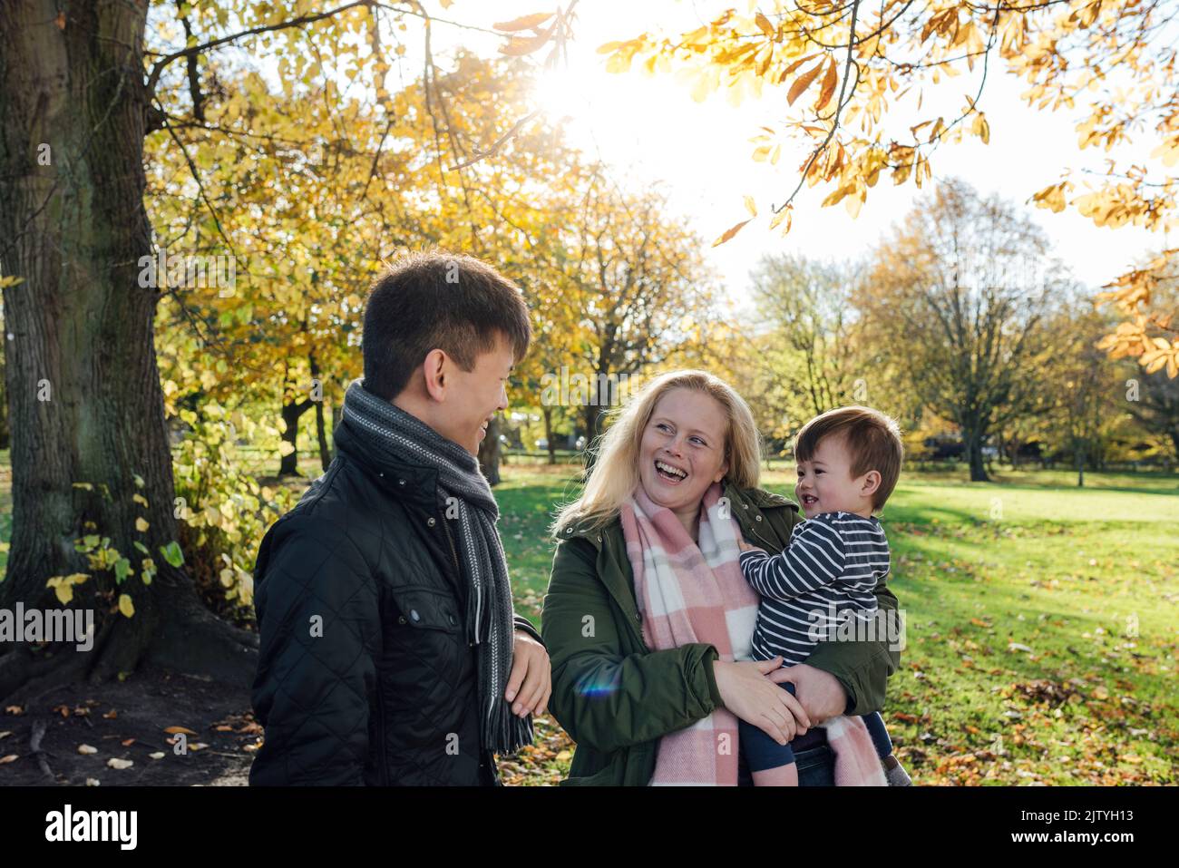 A family enjoying a day out in a public park together in Northumberland, North East England. The woman is carrying the baby boy while the man looks at Stock Photo