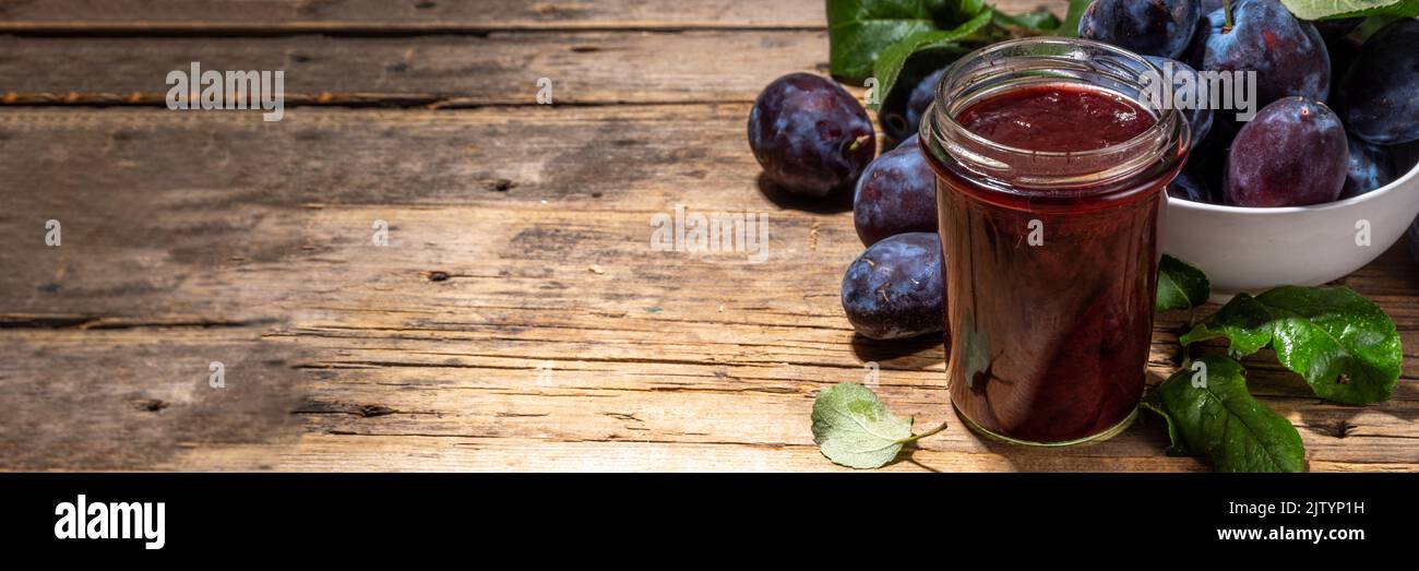 Red blue plum jam in small jar. Homemade autumn plum jam with fresh fruits. Fall preparations and canning on wooden table background copy space Stock Photo