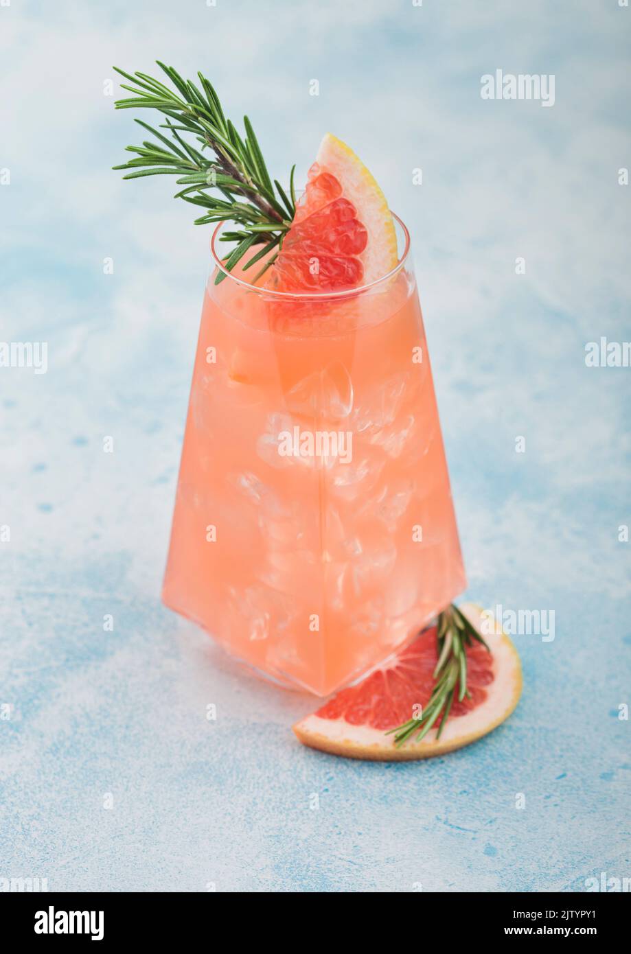 Cocktail with red grapefruit and vodka gin in modern luxury highball glass with fruit slice and rosemary on blue table background. Stock Photo