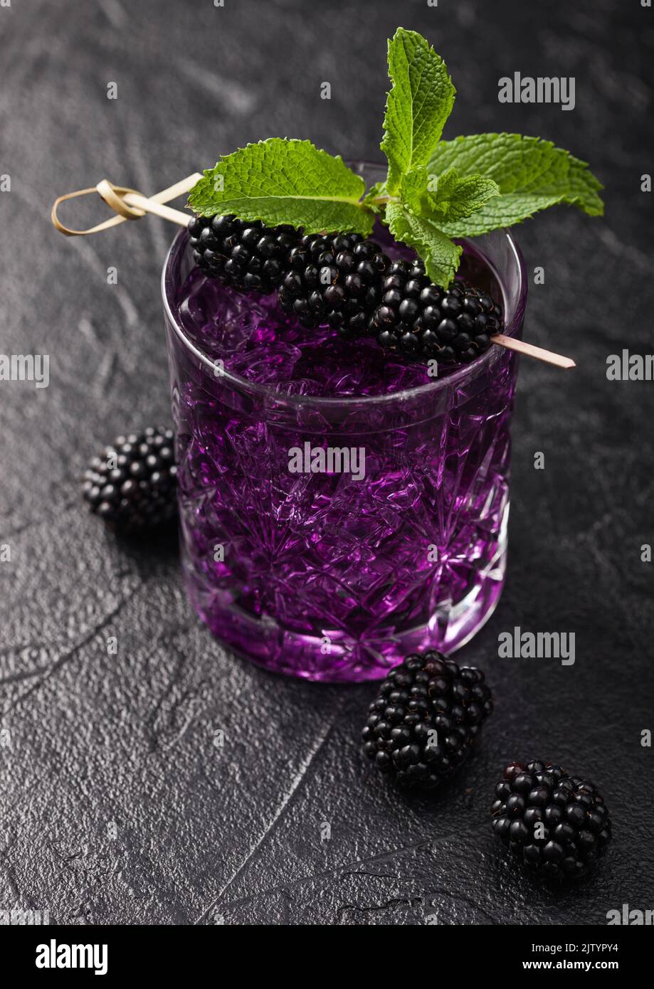 Blackberry refreshing summer cocktail in glass with ice and mint on black background with raw berries. Macro Stock Photo