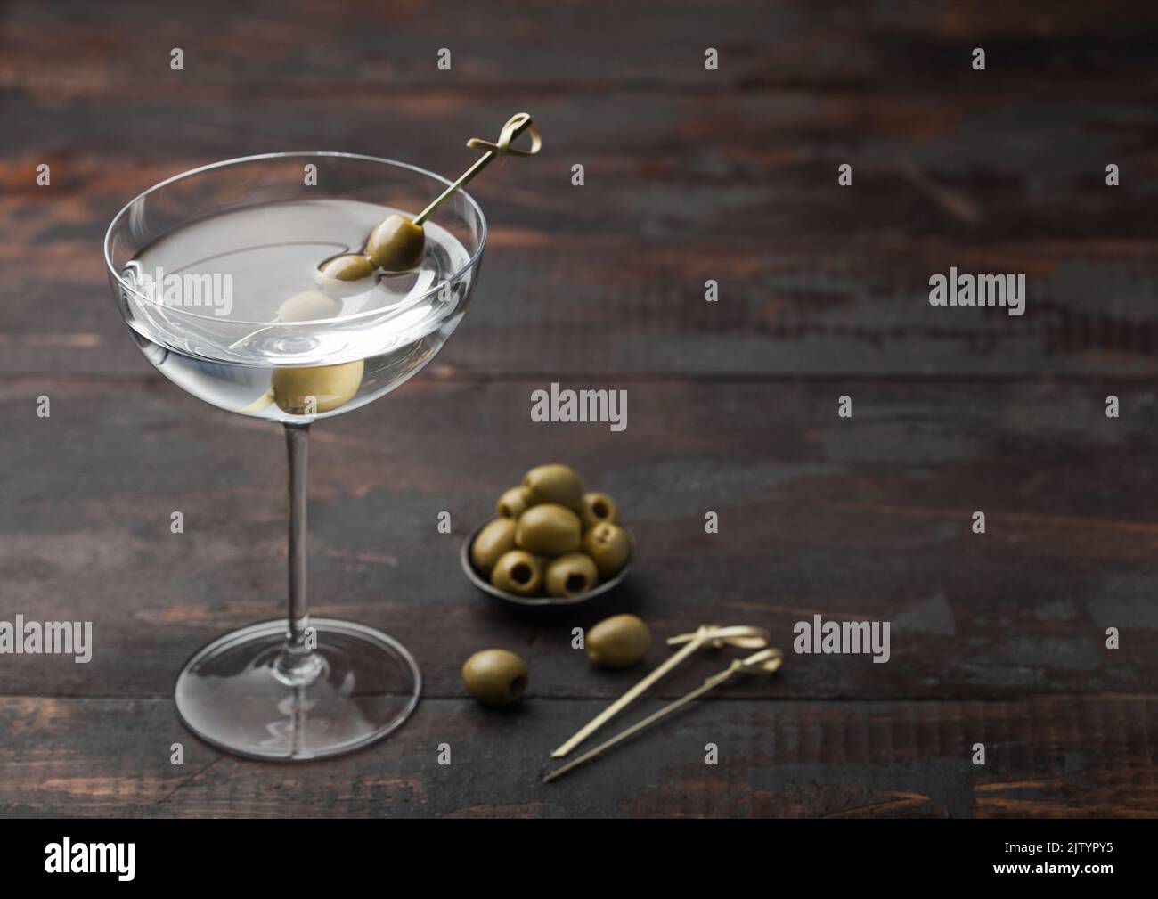 Vodka martini gin cocktail in modern glass with olives in metal bowl and bamboo sticks on dark wooden background. Space for text Stock Photo