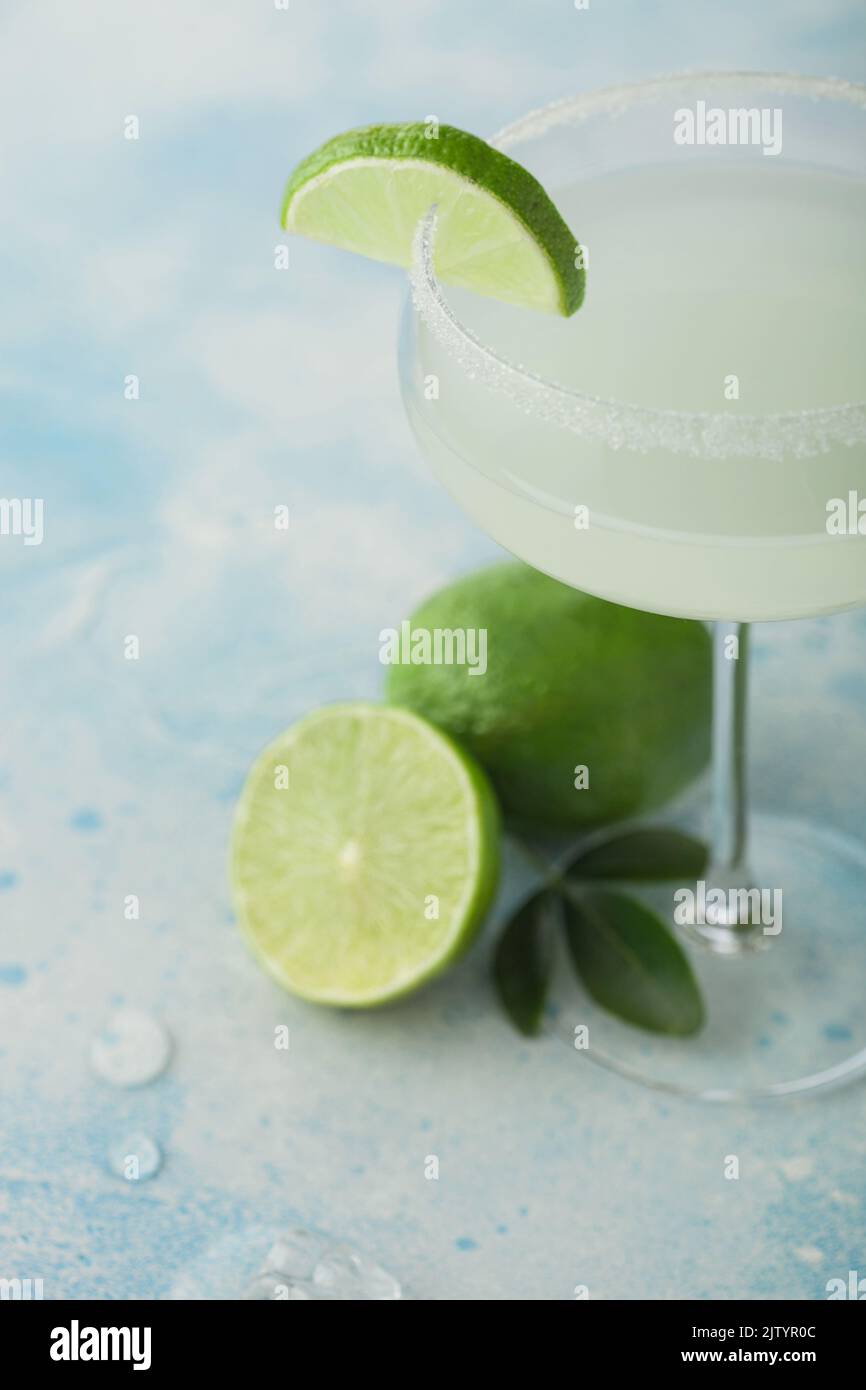 Crystal glass of Margarita cocktail with fresh limes on light blue table background. Macro Stock Photo