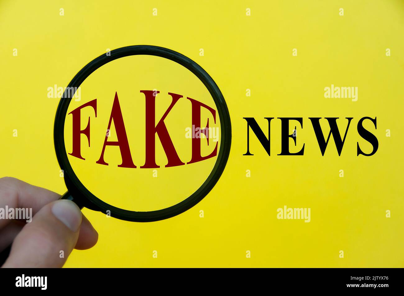 Close-up at fake news text through magnifying glass on yellow cover background. Fake news concept. Stock Photo