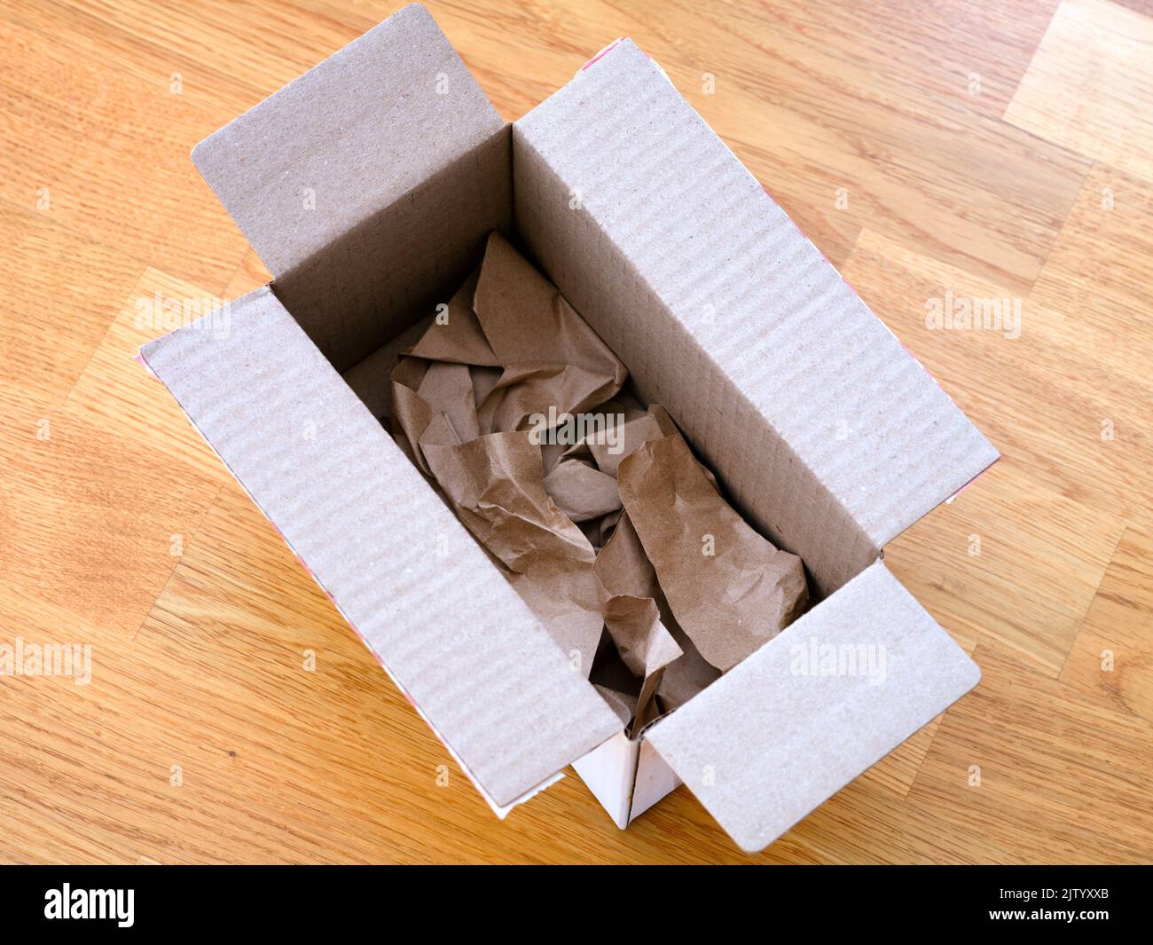 A cardboard box with paper inside on a parquet floor Stock Photo