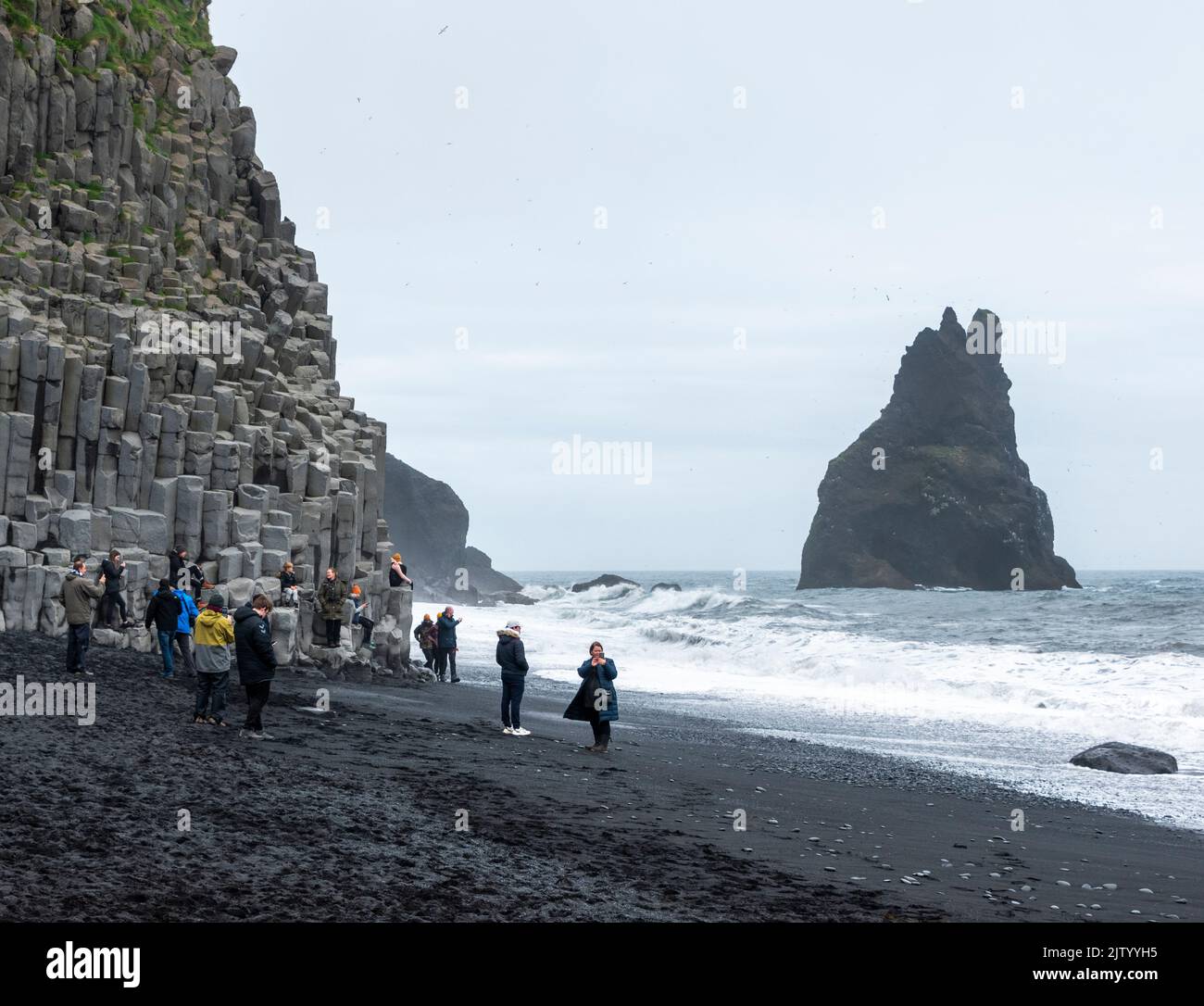 Tourists at Reynisfjara beach, climbing on the basalt columns and dodging the waves, Iceland. Stock Photo