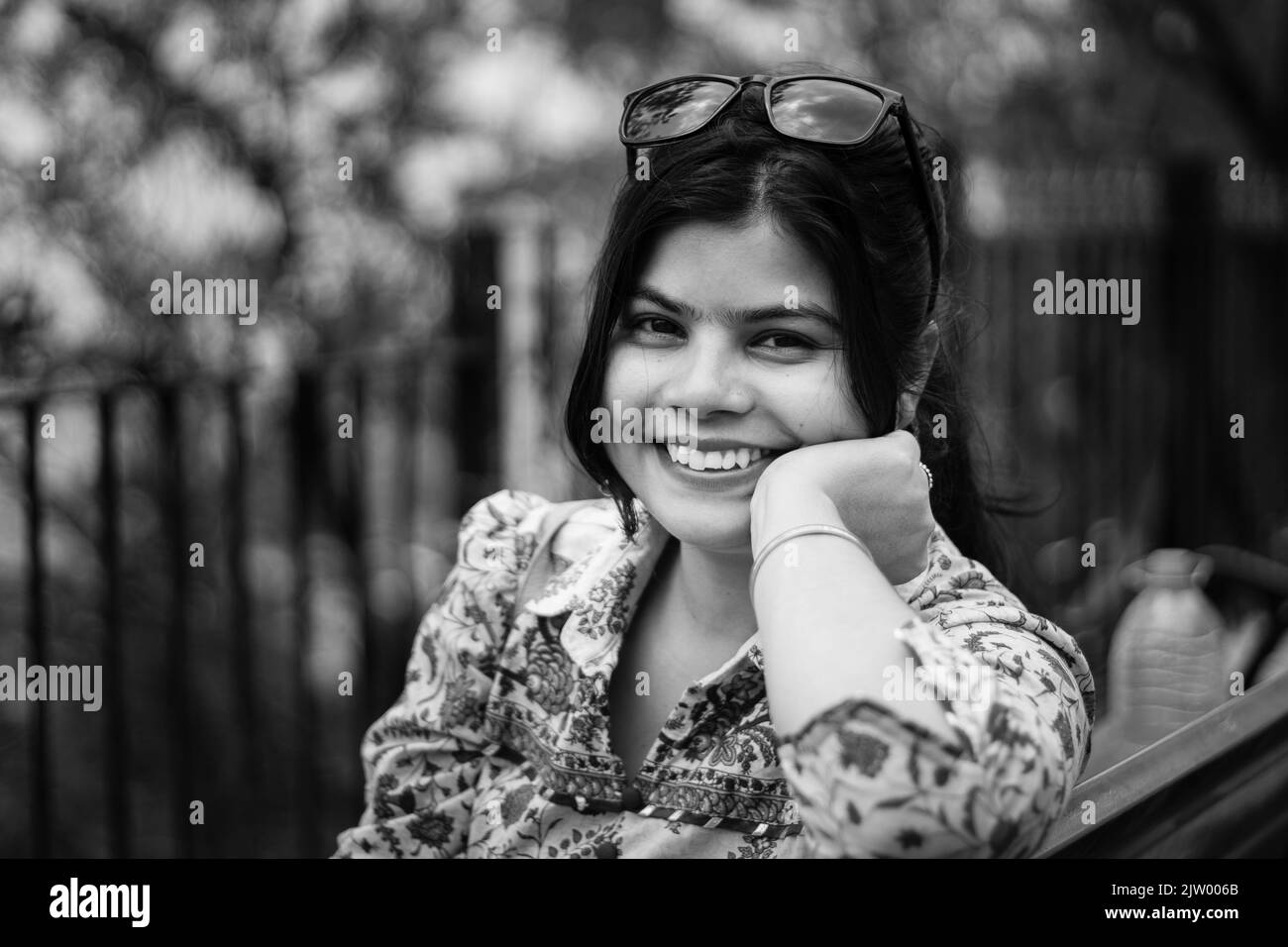 Black and white portrait of a pretty Indian woman with sunglasses on head smiling and looking at camera Stock Photo
