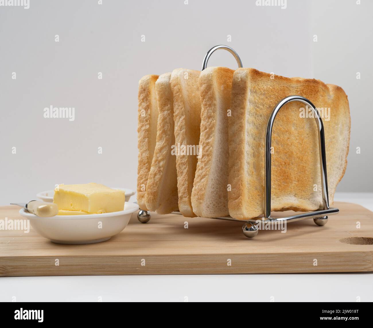Close up of chrome toast rack filled with white bread toast and bowl of buttter Stock Photo