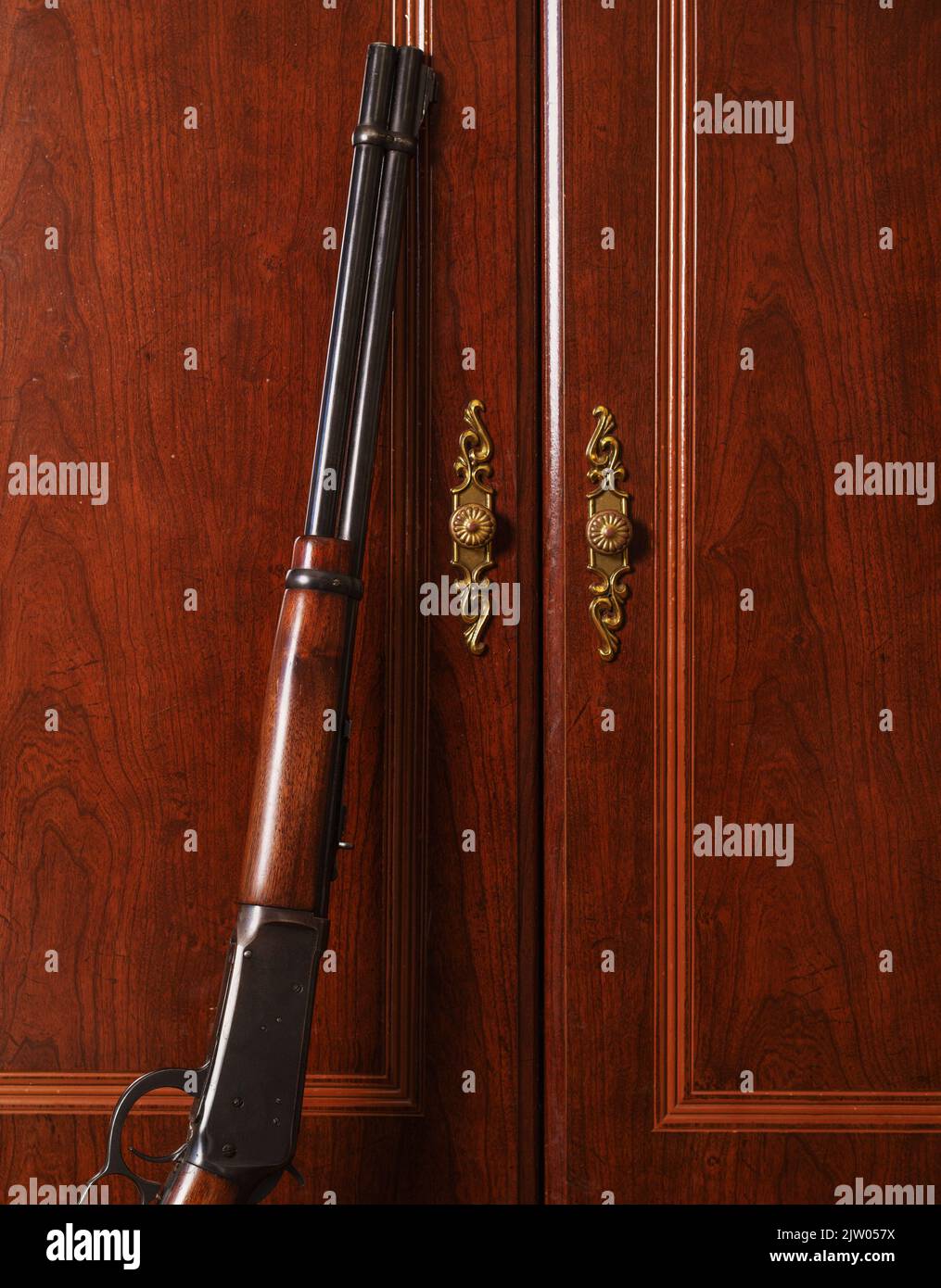 Classic lever-action rifle leaning against ornate dresser cabinet door Stock Photo