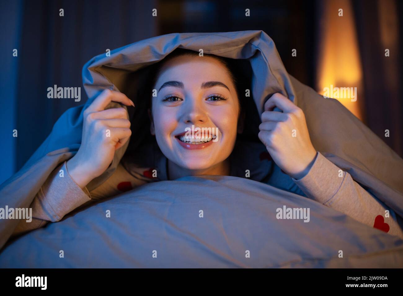 happy teenage girl lying under blanket in bed Stock Photo Alamy