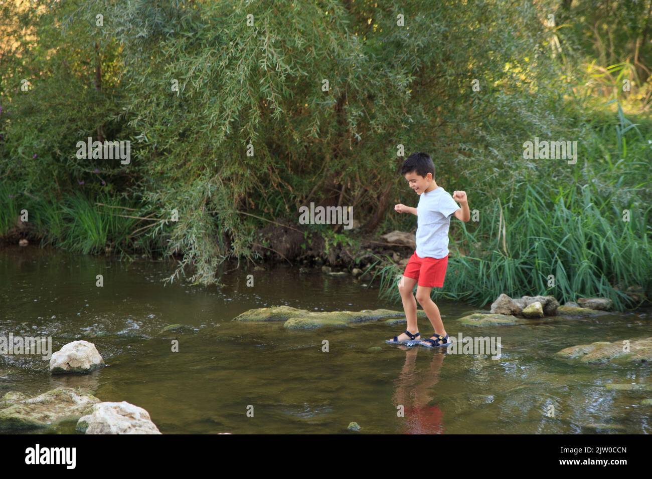 child crosses a river with a low riverbed in summer. Adventure games Stock Photo