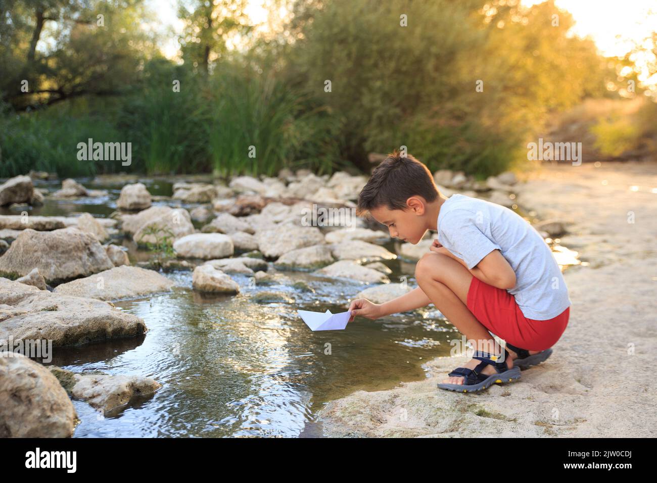 child plays with a paper boat in the river water in summertime Stock Photo