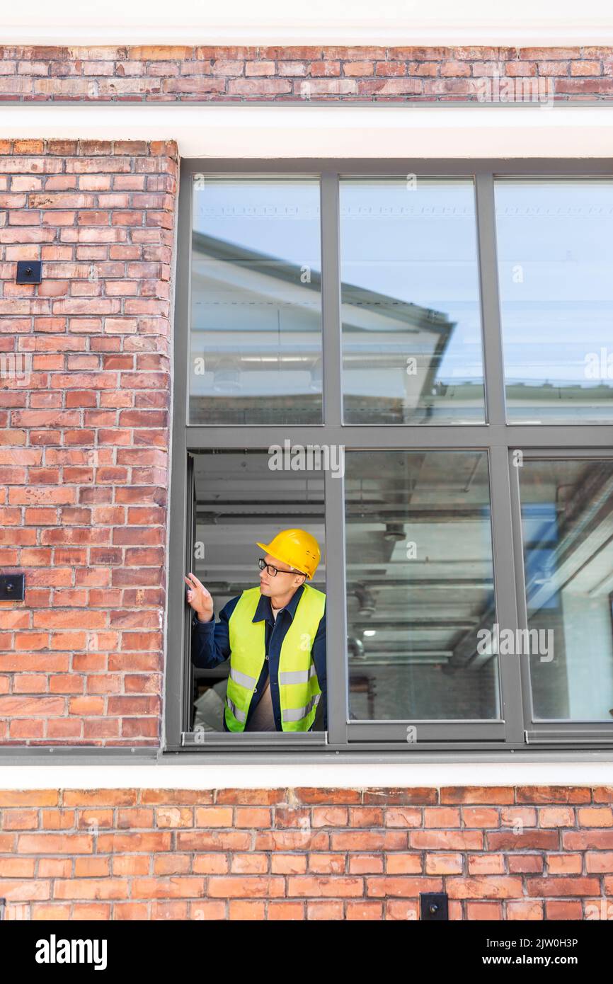 male builder in helmet looking out window Stock Photo
